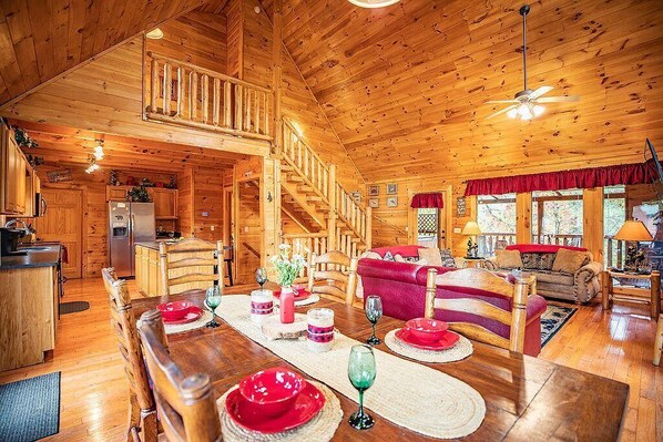 A wooden cabin interior with a dining area, kitchen, and living room.