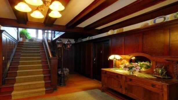 A grand staircase with a carpeted landing, a wooden console table with a lamp, and a view of the outdoors through a large window. - Petal Studio near DT, Free Parking (Victoria)