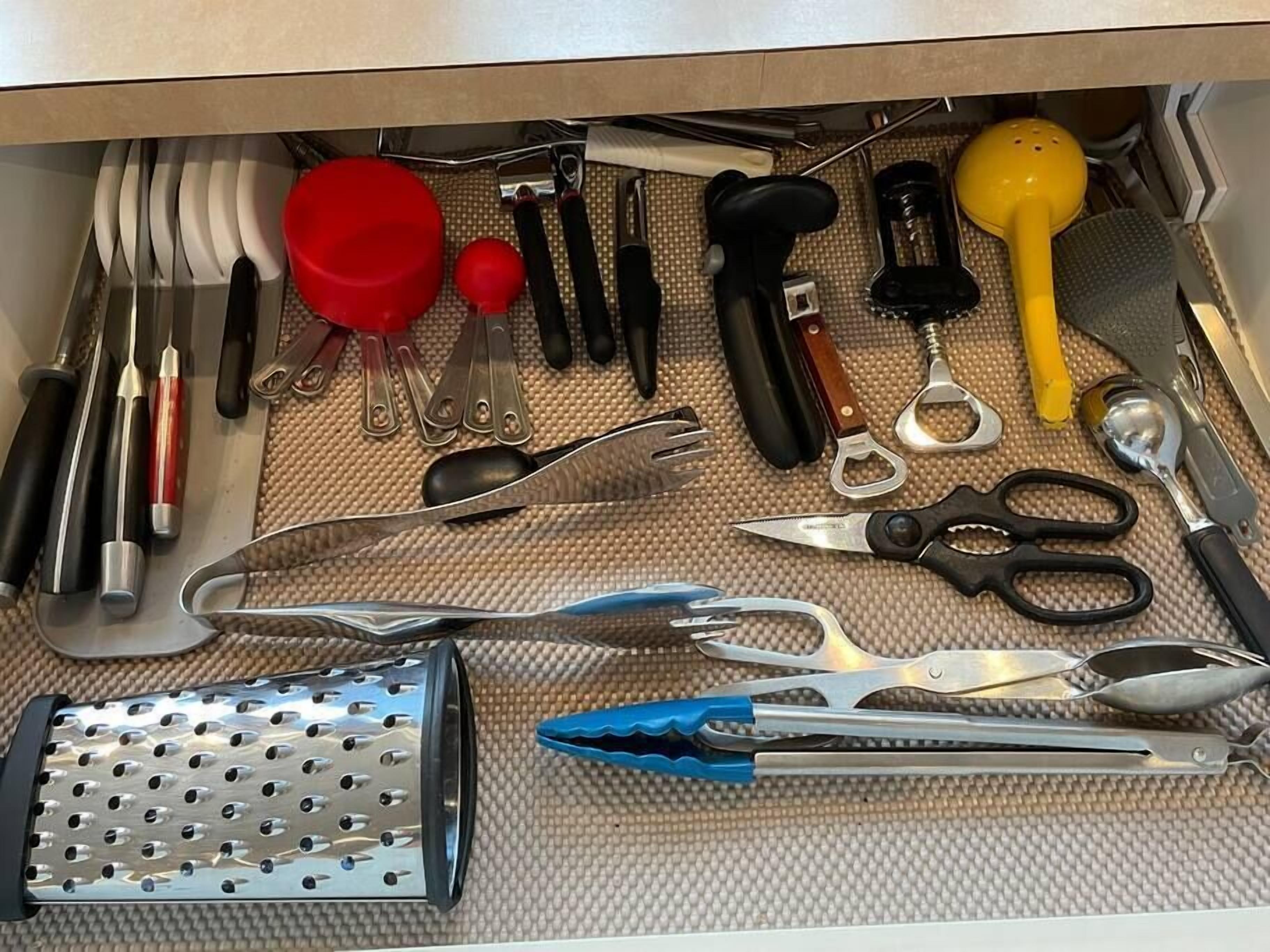 A drawer containing various kitchen utensils including a grater, scissors, and a yellow whisk.