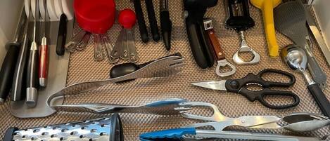 A drawer containing various kitchen utensils including a grater, scissors, and a yellow whisk.