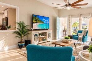 A living room with a television, a ceiling fan, a large potted plant, and a blue armchair. - 577 SunnyDaze | Private Heated Pool | Walk 2 Beach (Naples)