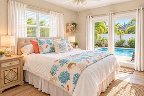 A bedroom with a large bed, a nightstand, a lamp, and a view of a swimming pool.