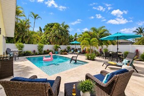 A backyard with a swimming pool, lounge chairs, and a flamingo float. - 577 SunnyDaze | Private Heated Pool | Walk 2 Beach (Naples)