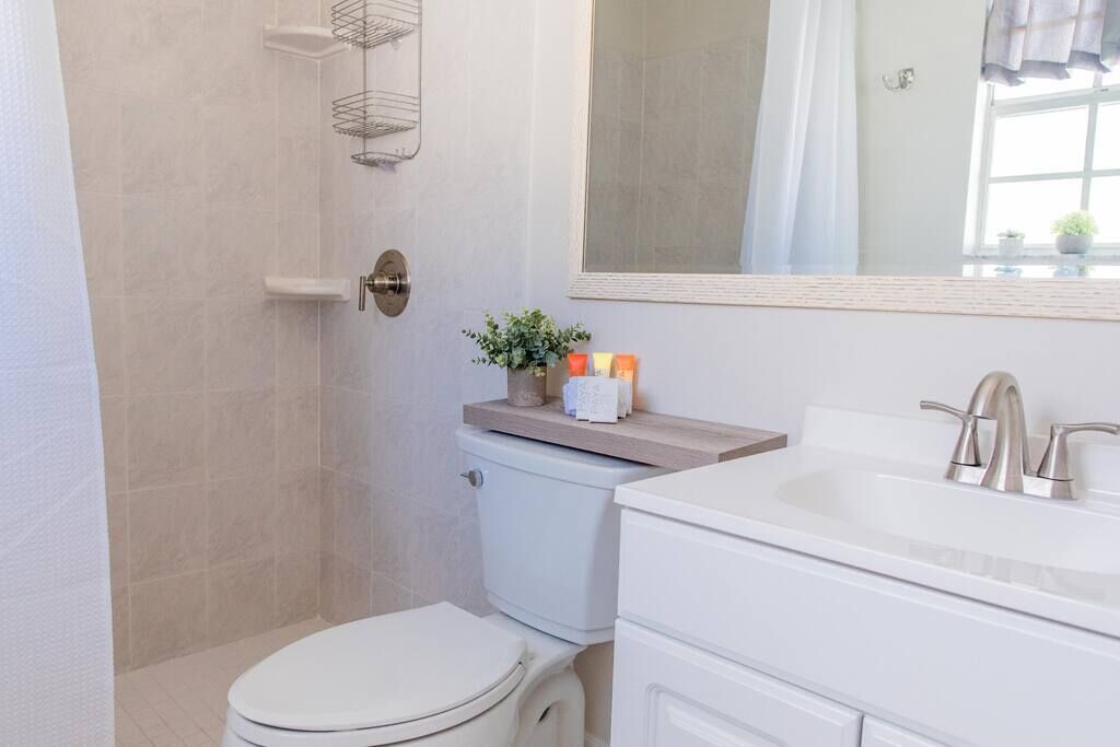 Une salle de bain comprenant des toilettes, un lavabo et un espace douche. On trouve des articles de toilette sur le comptoir du lavabo et un miroir au-dessus.