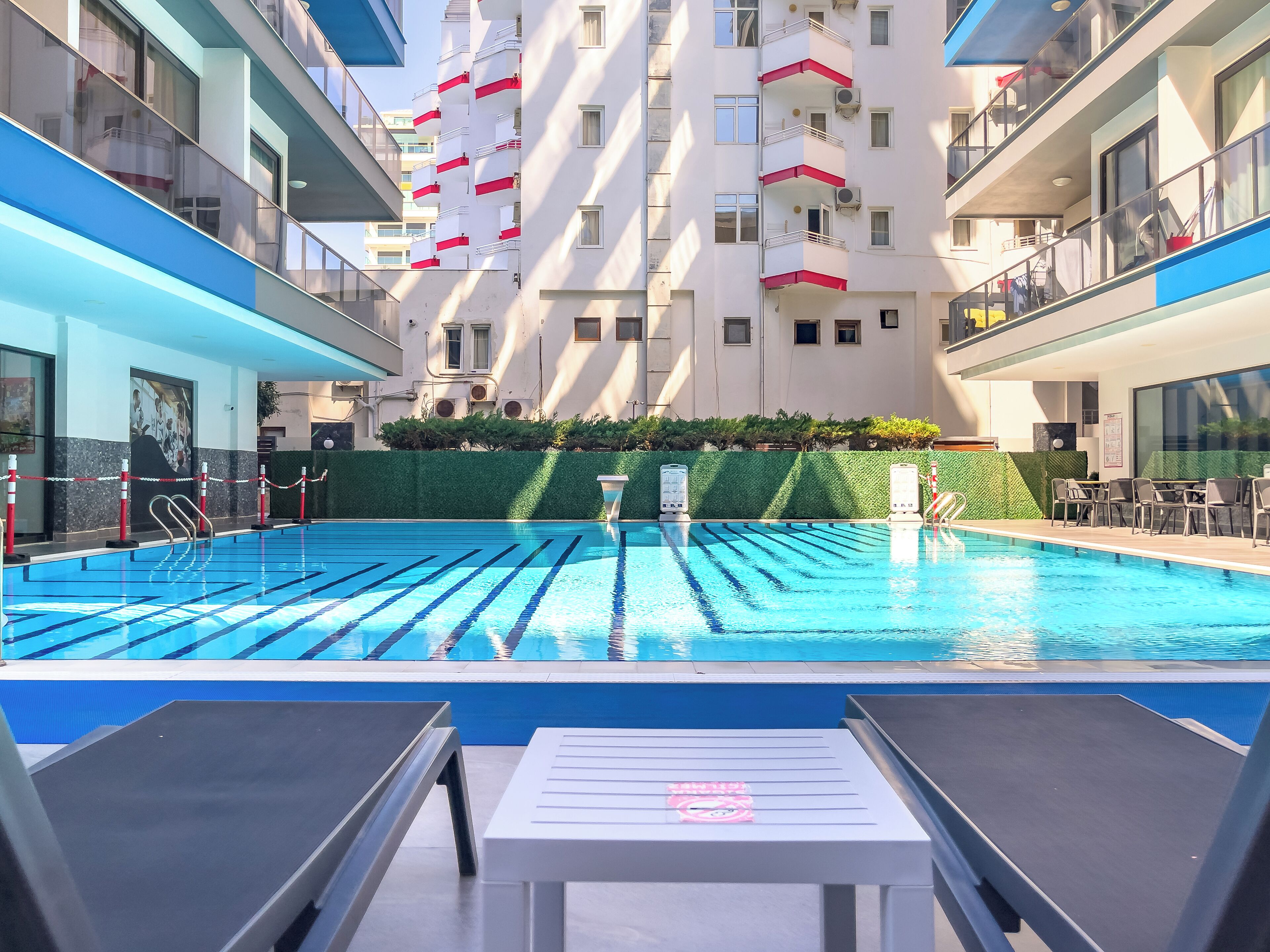 Ein Schwimmbecken mit Liegestühlen und einer Hecke im Hintergrund.