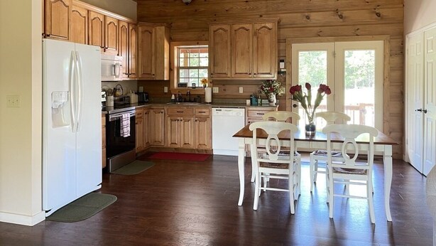 Una cocina con armarios de madera, un refrigerador, un microondas y una mesa de comedor con sillas.