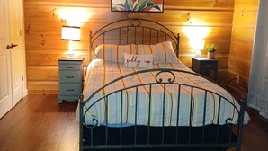 Un dormitorio con paneles de madera, una cama, dos mesitas de noche con lámparas, un ventilador de techo y un cuadro sobre la cama.
