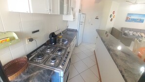 Une cuisine de taille réduite, avec des meubles blancs, une cuisinière à gaz, un évier et un réfrigérateur.