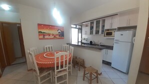 Une cuisine avec des meubles blancs, un réfrigérateur blanc et un coin repas comprenant une table et des chaises.
