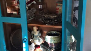 Un mueble color turquesa con puertas de cristal, que contiene varios objetos como una muñeca, un jarrón de vidrio y una caja de galletas.