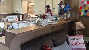 Una cocina con armarios blancos, un microondas y un lavamanos. Hay un muñeco de nieve decorativo y un árbol de Navidad en la encimera.