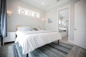 Une chambre à coucher comprenant un lit, des tables de chevet, une fenêtre ornée de motifs décoratifs, une salle de bain avec un miroir et une porte.