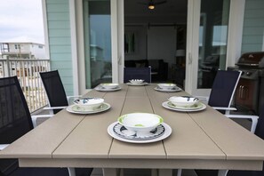 Une table à manger, dressée avec des assiettes et des bols, entourée de chaises, sur un balcon offrant une vue sur les bâtiments.