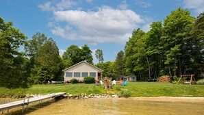 A lakeside cabin with a dock, surrounded by lush greenery and trees. - Round Lake Retreat: UP Lakefront Vacation Home (McMillan)