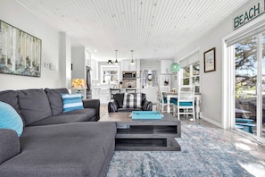 A modern living room with a grey sofa, a coffee table, and a dining area with white chairs.