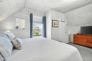 A bedroom with a large bed, a dresser, a TV, and a window with a view.