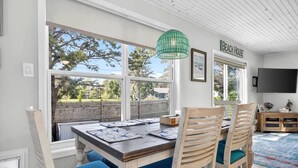 Un espace repas comprenant une table, des chaises, un luminaire suspendu vert, un téléviseur et une vue sur le jardin arrière.