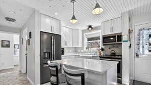 Une cuisine moderne avec des meubles blancs, un grand îlot central, des appareils électroménagers en acier inoxydable et des luminaires suspendus.