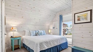 Une chambre à coucher avec un lit, une table de chevet, une lampe, une fenêtre donnant sur un beau paysage et un tableau encadré accroché au mur.