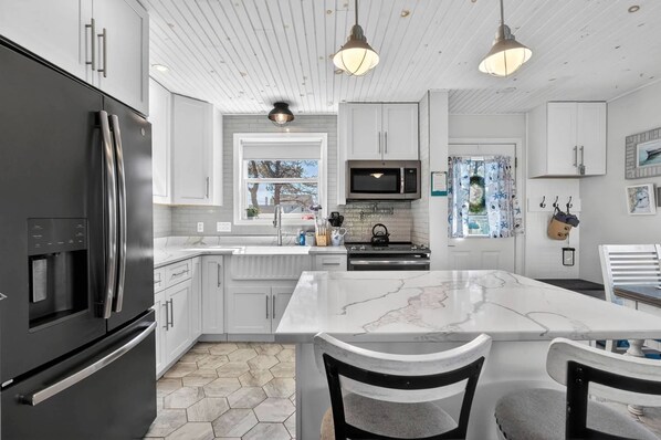 A modern kitchen with white cabinetry, a large island, stainless steel appliances, and pendant lighting.