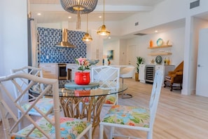 A modern kitchen with a blue mosaic backsplash, white cabinetry, and a dining area with a glass table and wicker chairs. - 606 SeaRenity Resort • Designer Home w/Heated Pool (Naples)