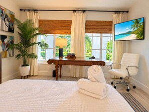 Een hotelkamer met een bed, een bureau, een stoel, een kamerplant en een televisie aan de muur.