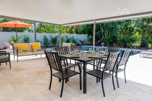 An outdoor patio with a pool, dining table, and chairs.