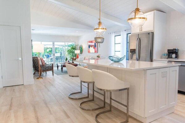 A modern kitchen with a central island, bar stools, stainless steel appliances, and pendant lighting. - 606 SeaRenity Resort • Designer Home w/Heated Pool (Naples)