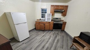 A compact kitchen with a refrigerator, microwave, stove, and wooden cabinets. - Green Garden Inn (Greensboro)