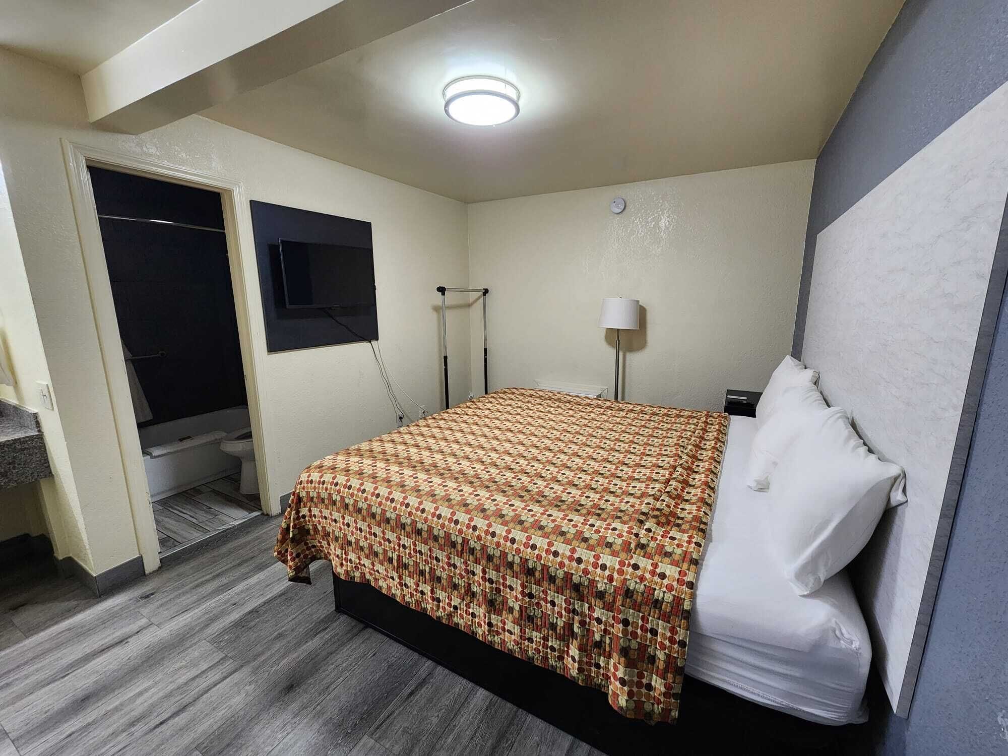 A bedroom with a bed, a bedside lamp, a window, and a door leading to a bathroom.