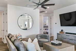 A modern living room with a ceiling fan, a round mirror, a gray armchair, a sofa with patterned cushions, and a flat-screen TV on the wall. - Ace on the 8th by RedAwning (Washington)