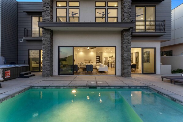 Une maison moderne à deux étages, dotée d’une piscine, de grandes fenêtres et d’un jacuzzi.