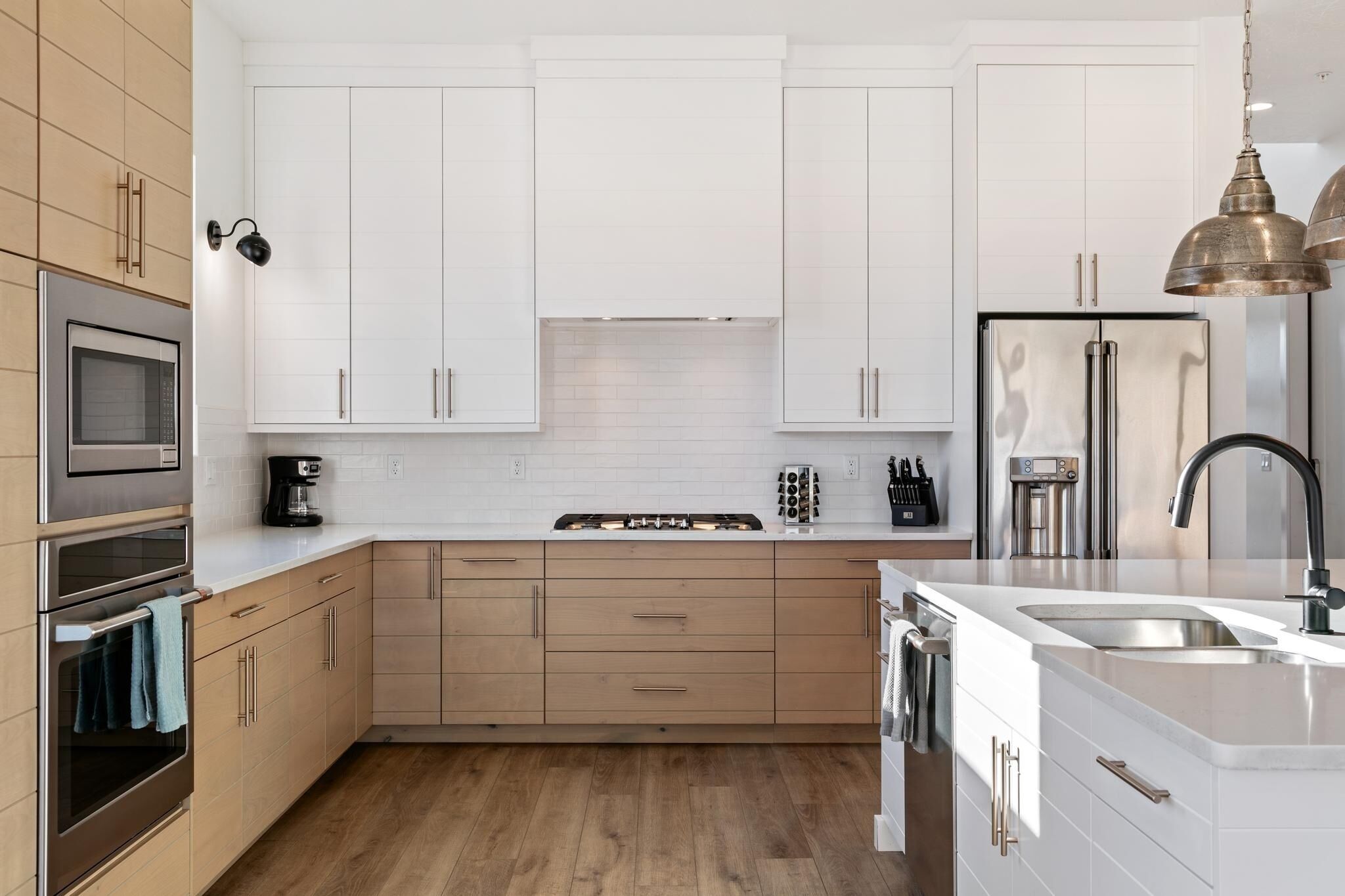 Une cuisine moderne avec des armoires blanches, des appareils en acier inoxydable et un plancher en bois.