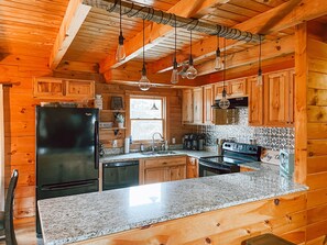 A kitchen with wooden cabinets, a black refrigerator, a granite countertop, and hanging light fixtures.