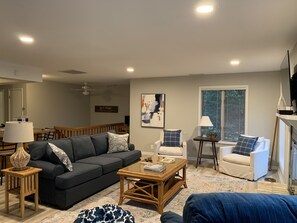 A living room with a dark grey sofa, a white armchair, a wooden coffee table, and a patterned rug.