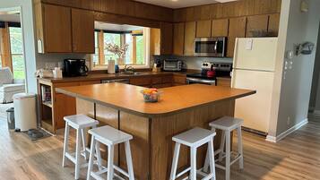 Una cocina moderna con armarios de madera, una isla central con taburetes, electrodomésticos de acero inoxidable y un amplio ventanal que proporciona luz natural.