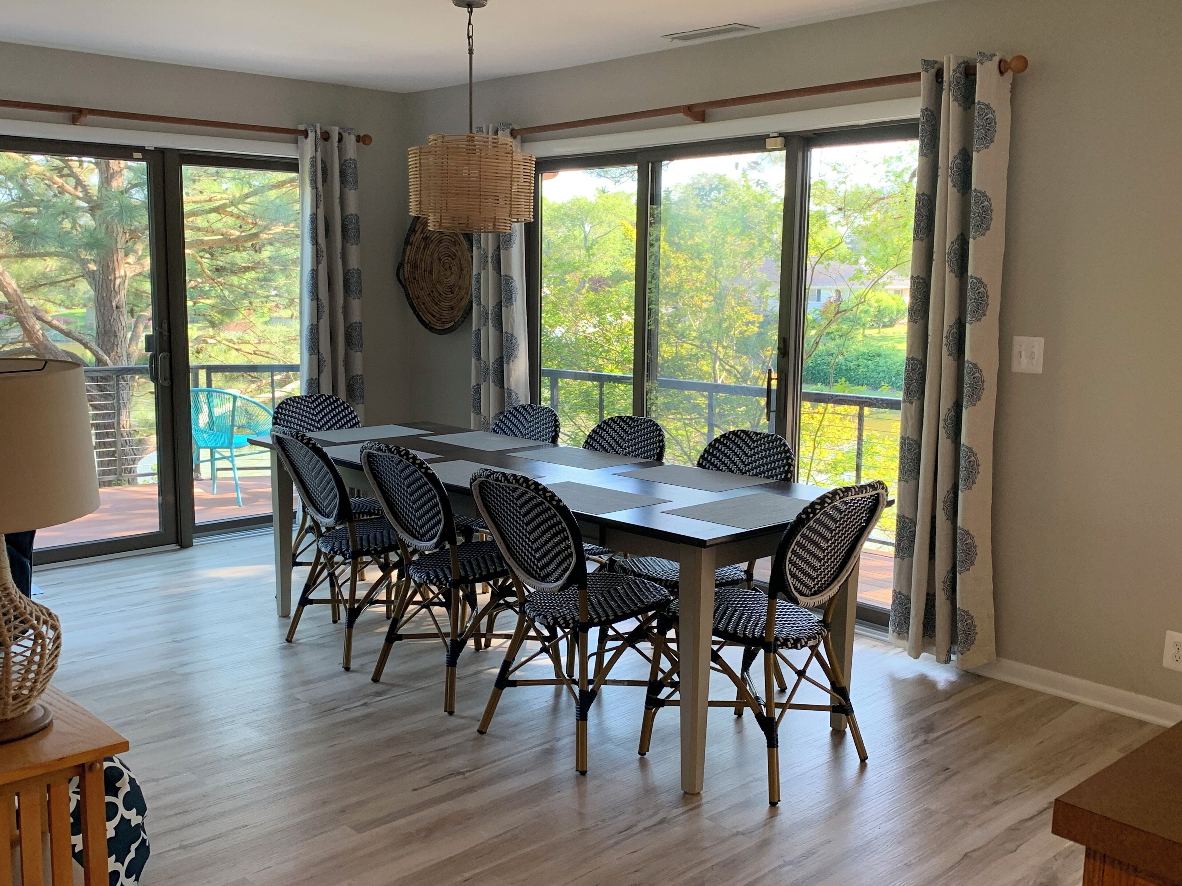 Un espace repas comprenant une grande table et six chaises, de grandes fenêtres avec des rideaux et un luminaire suspendu.