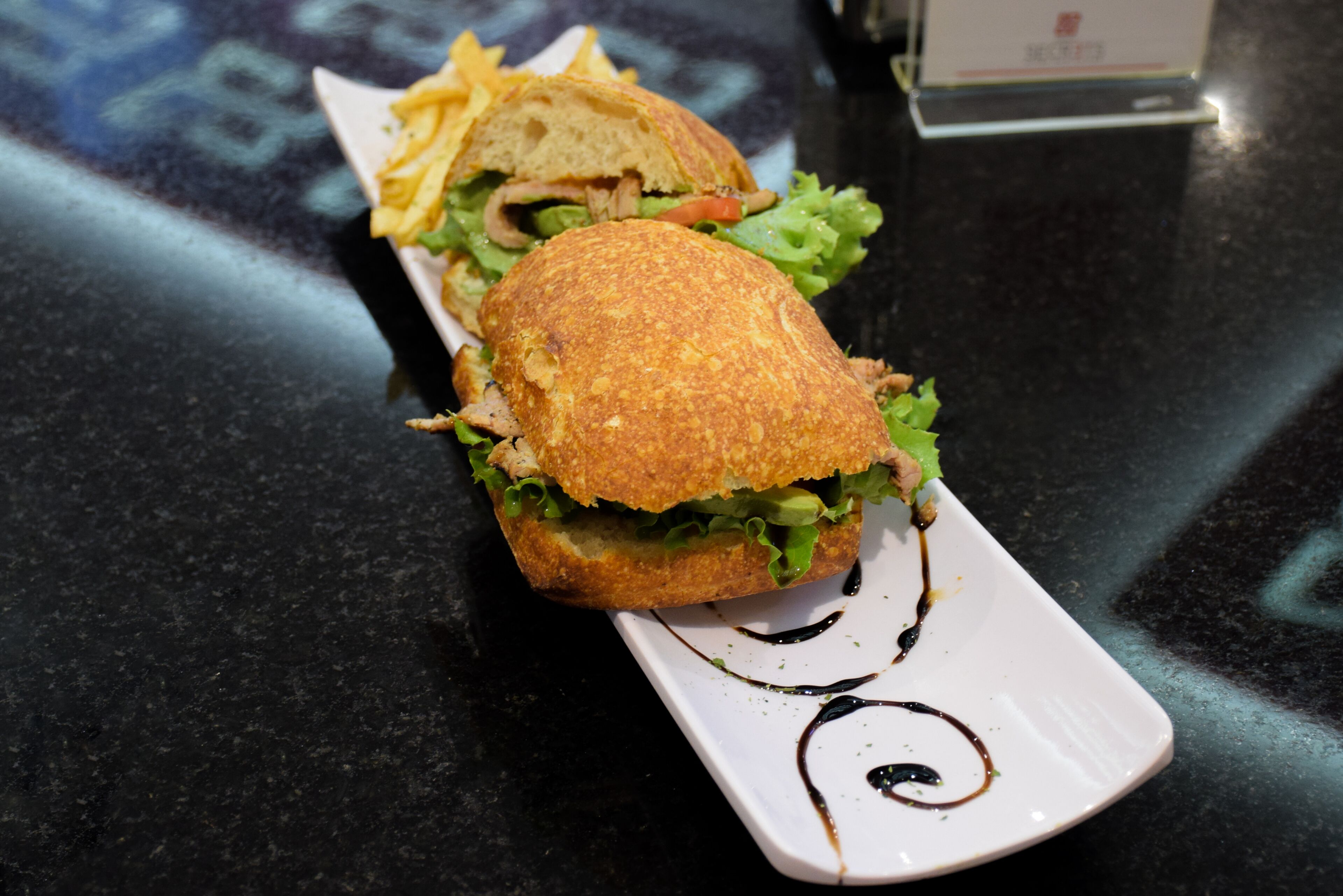 Un sandwich sur une assiette blanche, nappé d’une fine couche de sauce.
