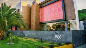 A modern building with a large red patterned facade, a number '806' on the wall, and a well-maintained garden with palm trees. - Hotel Passion Secrets Villas & Suites (Toluca)