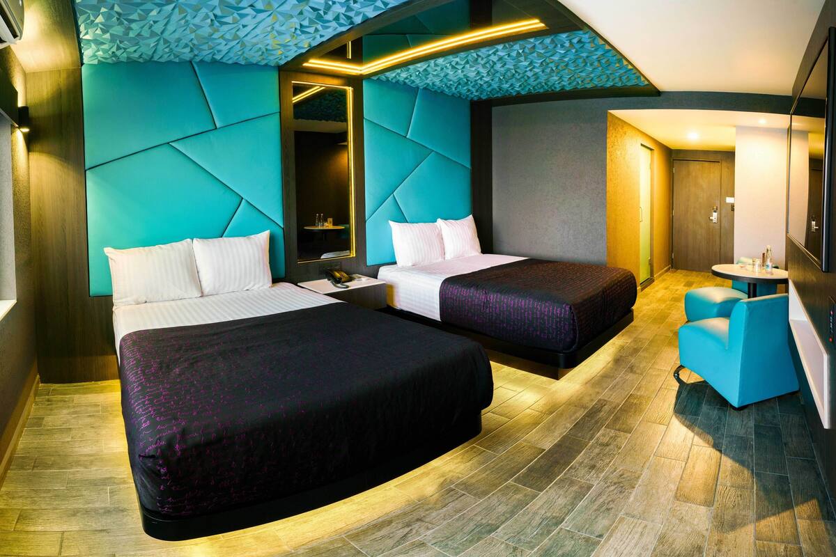 Een moderne hotelkamer met twee bedden, een zithoek en een grote spiegel.