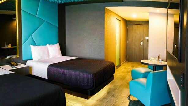 A modern hotel room with a large bed, a smaller bed, a desk with a phone, and a seating area with a table and chairs. - Hotel Passion Secrets Villas & Suites (Toluca)