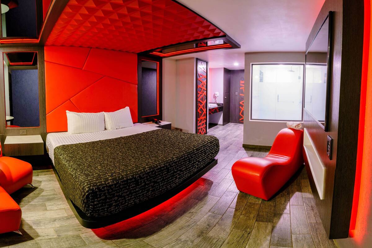 Een moderne hotelkamer met een groot bed, rode accenten, een zithoek en uitzicht op de stad.
