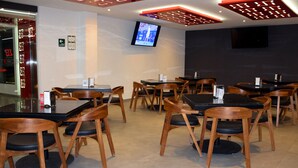 A restaurant with multiple tables and chairs, a TV mounted on the wall, and a glass door entrance. - Hotel Passion Secrets Villas & Suites (Toluca)