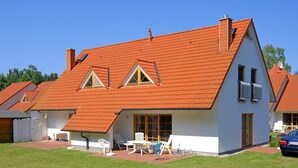 A two-story house with a red-tiled roof, two dormer windows, and a small patio with outdoor furniture. - Spacious semi-detached house with garden, terrace and pool in the Zingst vacation park - (Zingst)