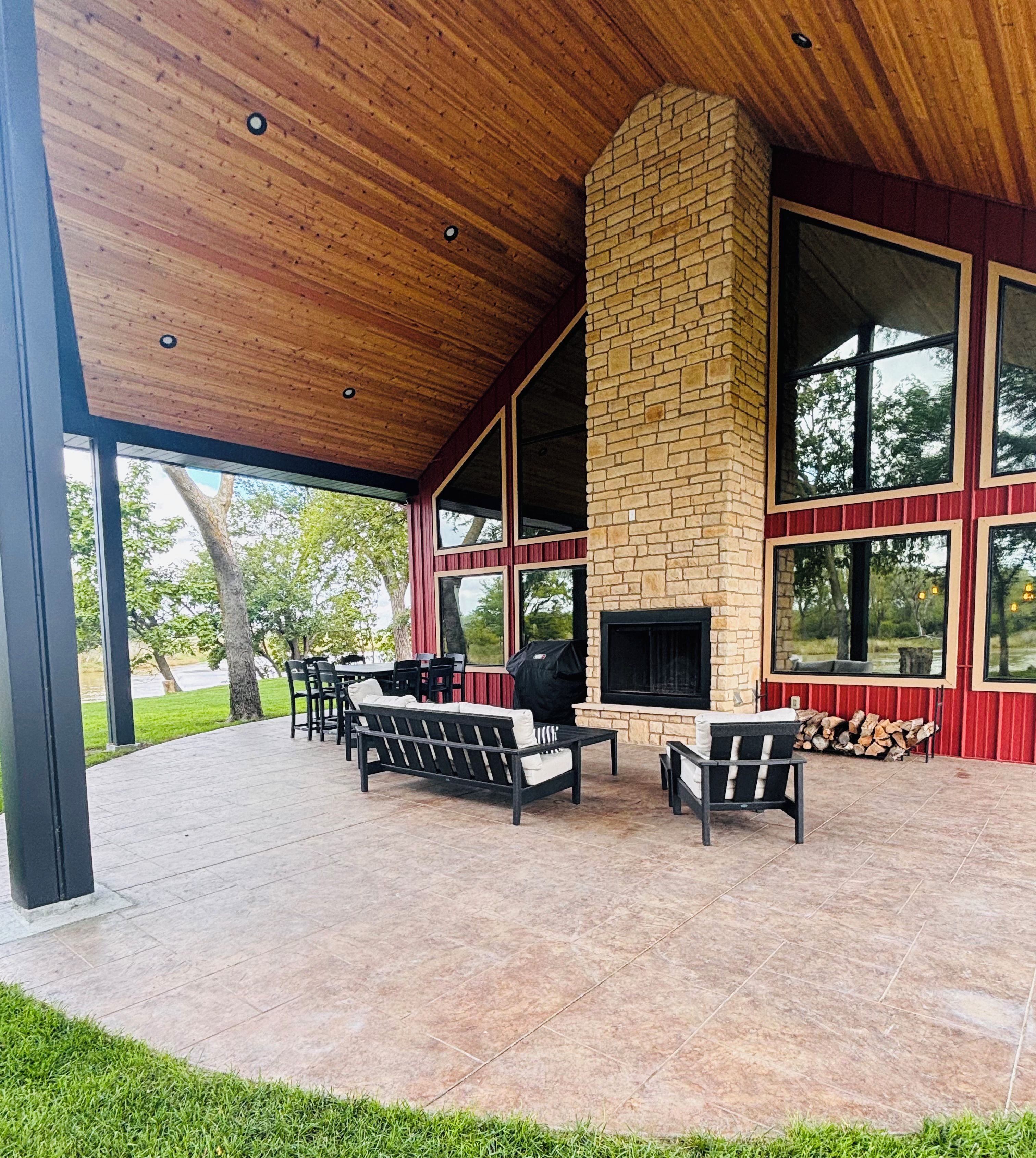 An outdoor patio with a stone fireplace, seating area, and large windows.