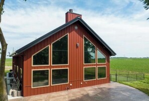 En röd byggnad av metall med stora fönster och en skorsten, belägen på en betonguppfart med en gräsyta i bakgrunden.