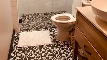 A bathroom with a toilet, a sink, a shower area, and a patterned floor.