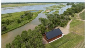 Una casa con techo rojo y amplios ventanales, rodeada de césped y un río.