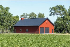 A red barn with a black roof, two garage doors, and a fenced field in the foreground. - Sandhill Crane viewing experience of a lifetime in Nebraska on the Platte River! (Gibbon)