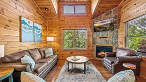 Un intérieur chaleureux de chalet en bois, avec une cheminée, des canapés en cuir et un mur décoratif en pierre.